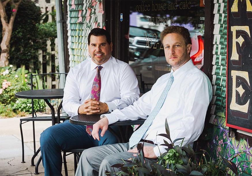 Two businessmen sitting outside a coffee shop in casual conversation.
