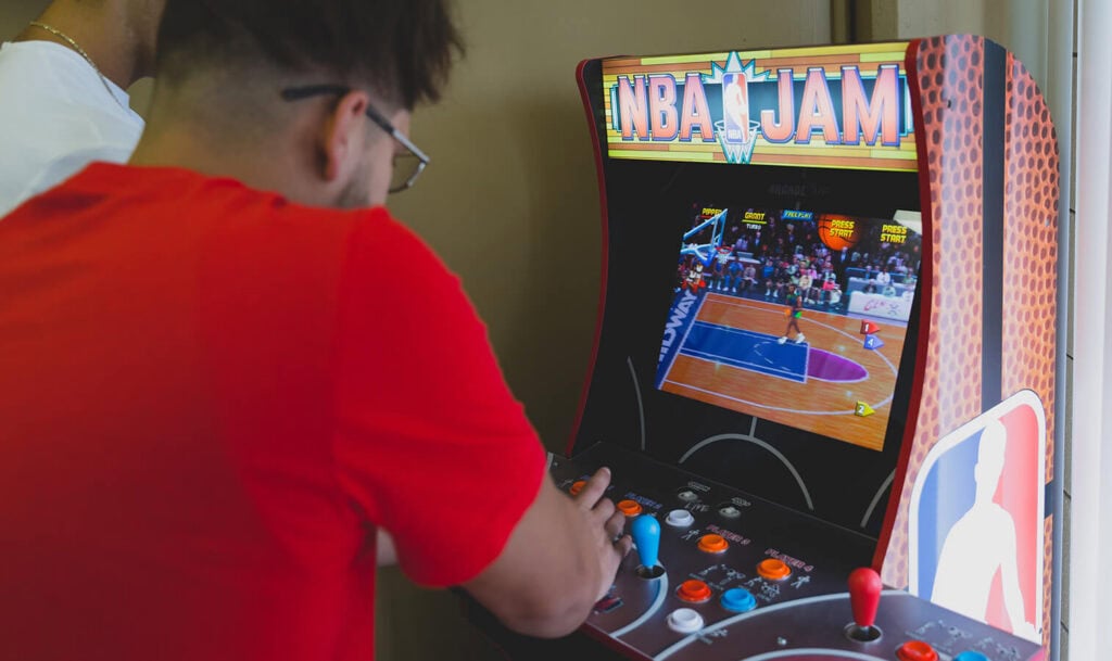Person playing NBA Jam arcade game at NOLA Detox campus.
