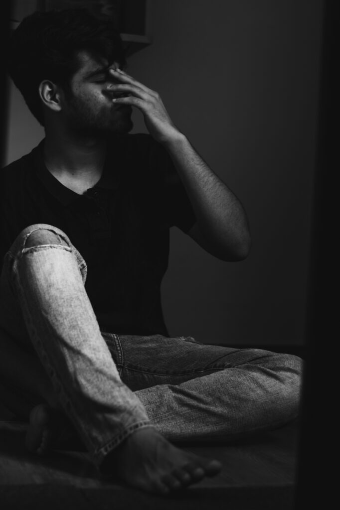 Young man sitting with hand on face, showing signs of stress or anxiety.