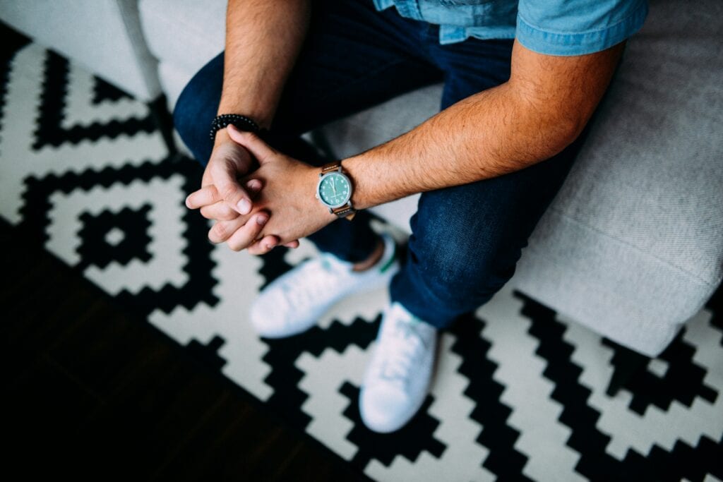 Man sitting on sofa with hands clasped, symbolizing anxiety or stress.