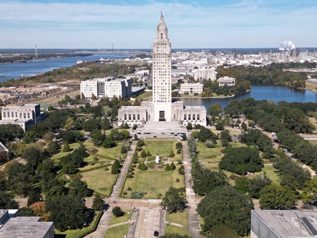 Aerial view of the Louisiana State Capitol in Baton Rouge with surrounding gardens and river.