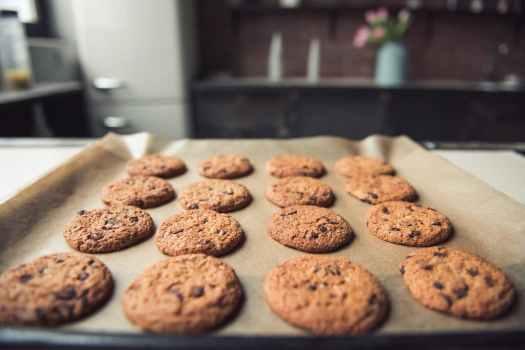 Freshly baked chocolate chip cookies on baking sheet in kitchen.