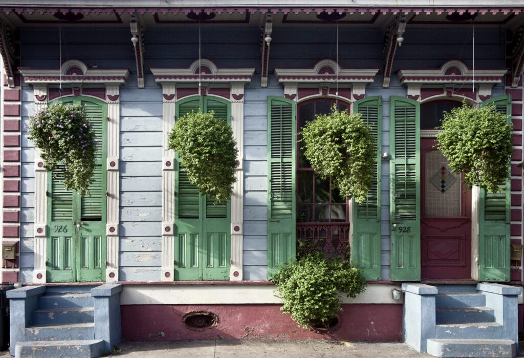 Colorful New Orleans house with green shutters and potted plants.