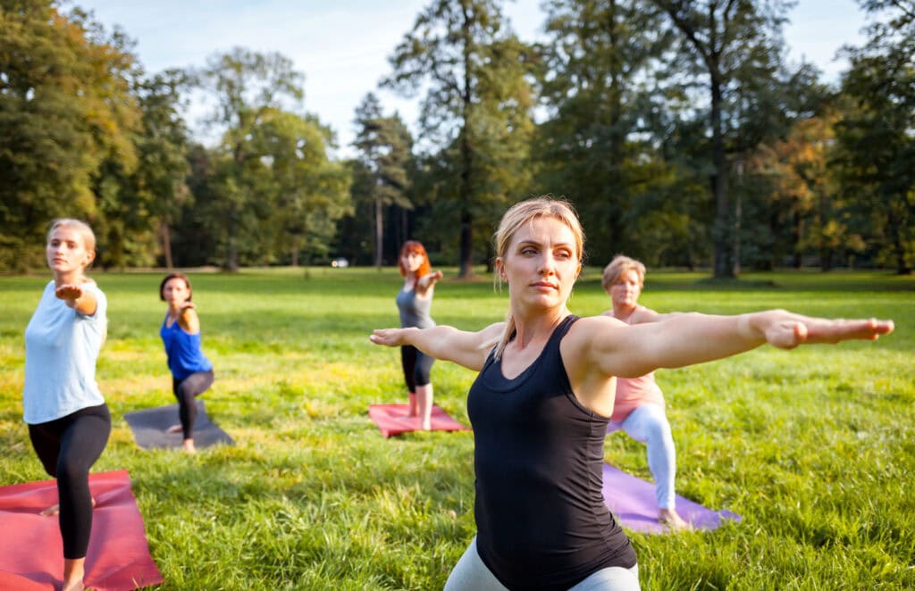 Group of people practicing outdoor yoga in a park with trees and grass.