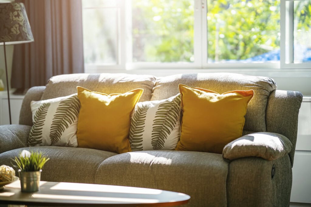 Cozy living room with beige sofa and yellow accent pillows near window.